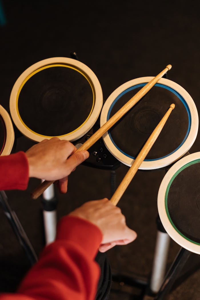 Hands playing electronic drum pad set with colored rings.