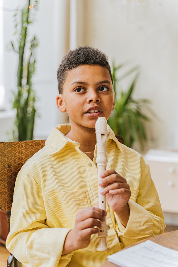 Young boy learning to play the recorder at home, wearing a yellow shirt.