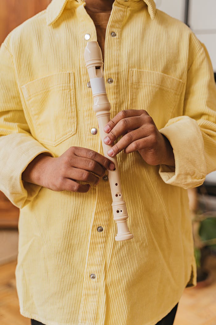 Close-up of hands holding a white recorder, wearing a yellow shirt indoors.