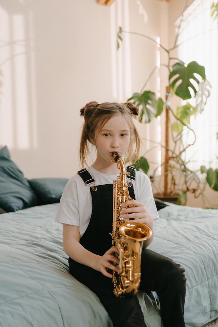 about-us-02 A young girl sits on a bed playing a saxophone, surrounded by a warm, cozy interior with plants.